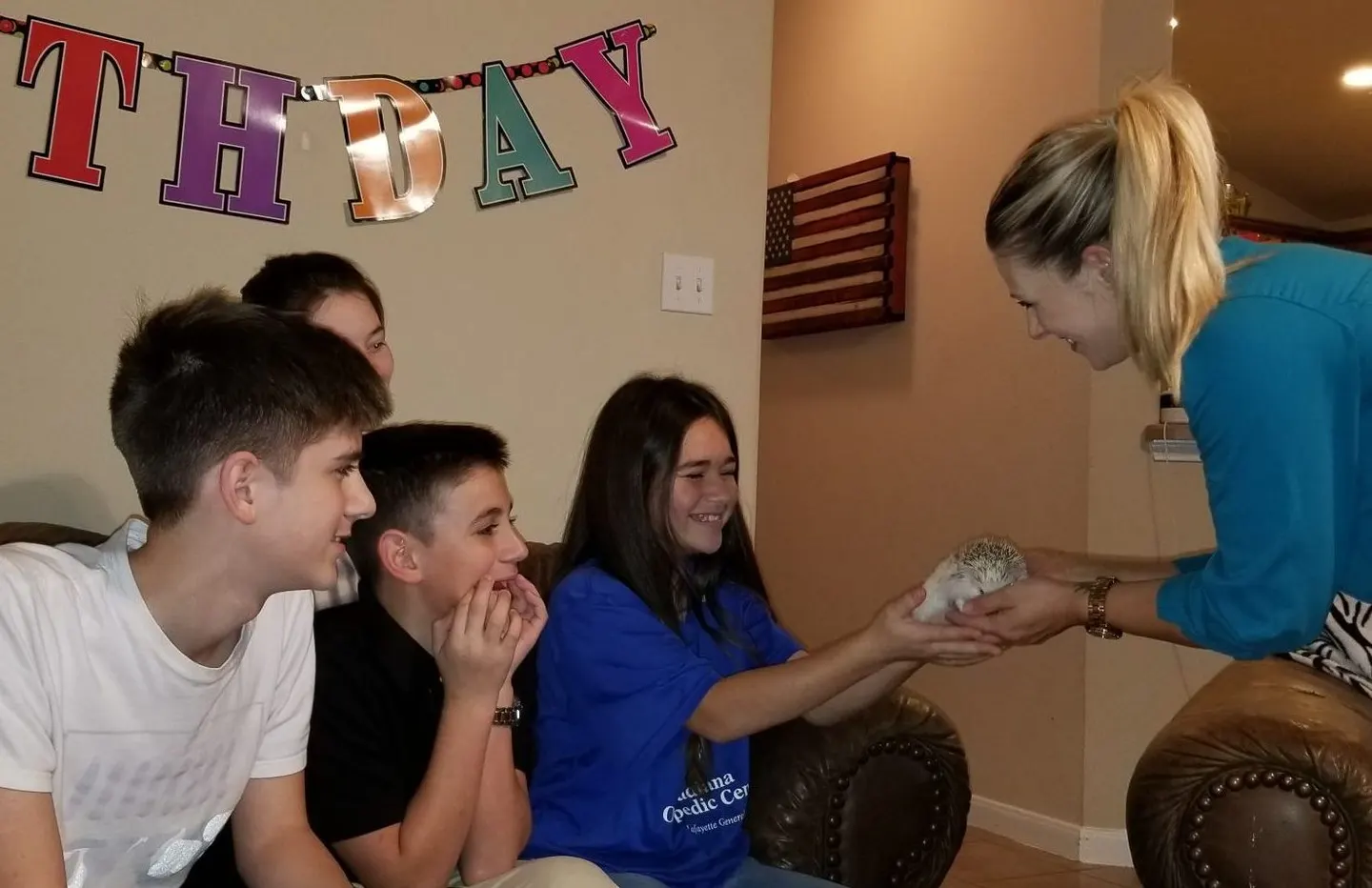 A handler shows a small animal to a group of teenagers at an off-site birthday party.